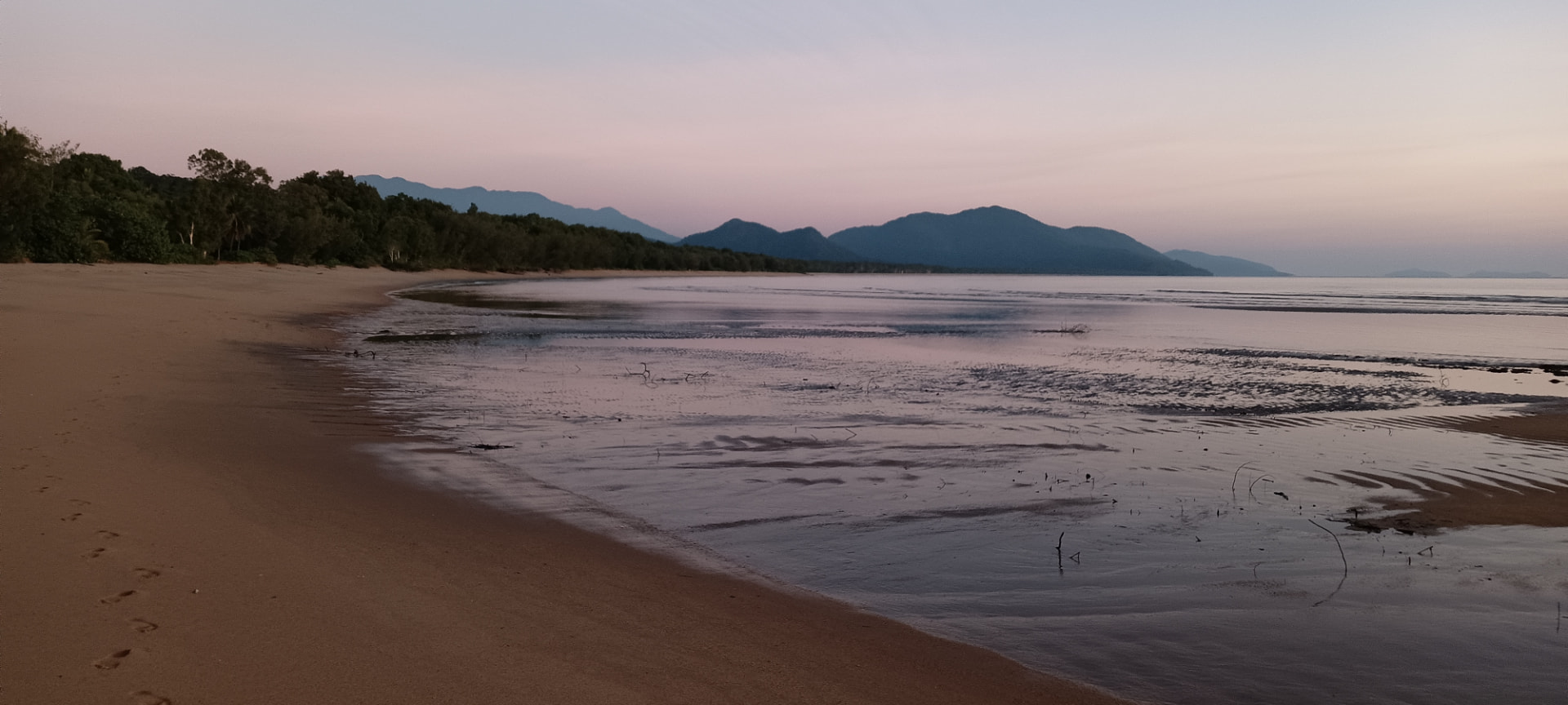 Quiet Bramston Beach shoreline and rainforest mountains at twilight
