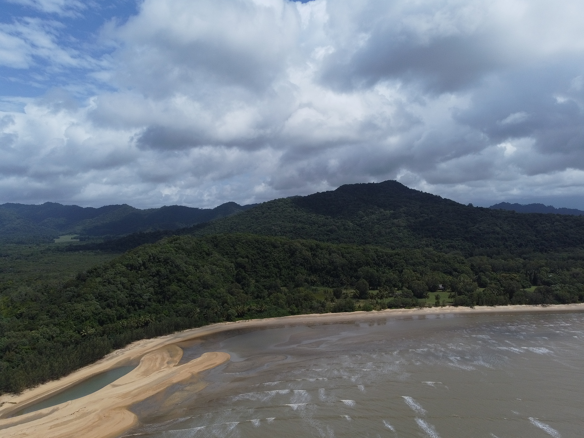 Aerial view of Bramston Beach shoreline and tropical mountains under clouds
