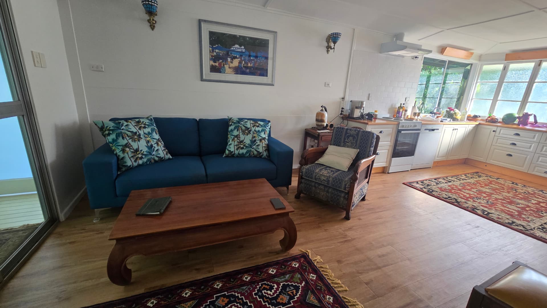 Sunlit lounge with palm-print cushions and open kitchen beyond
